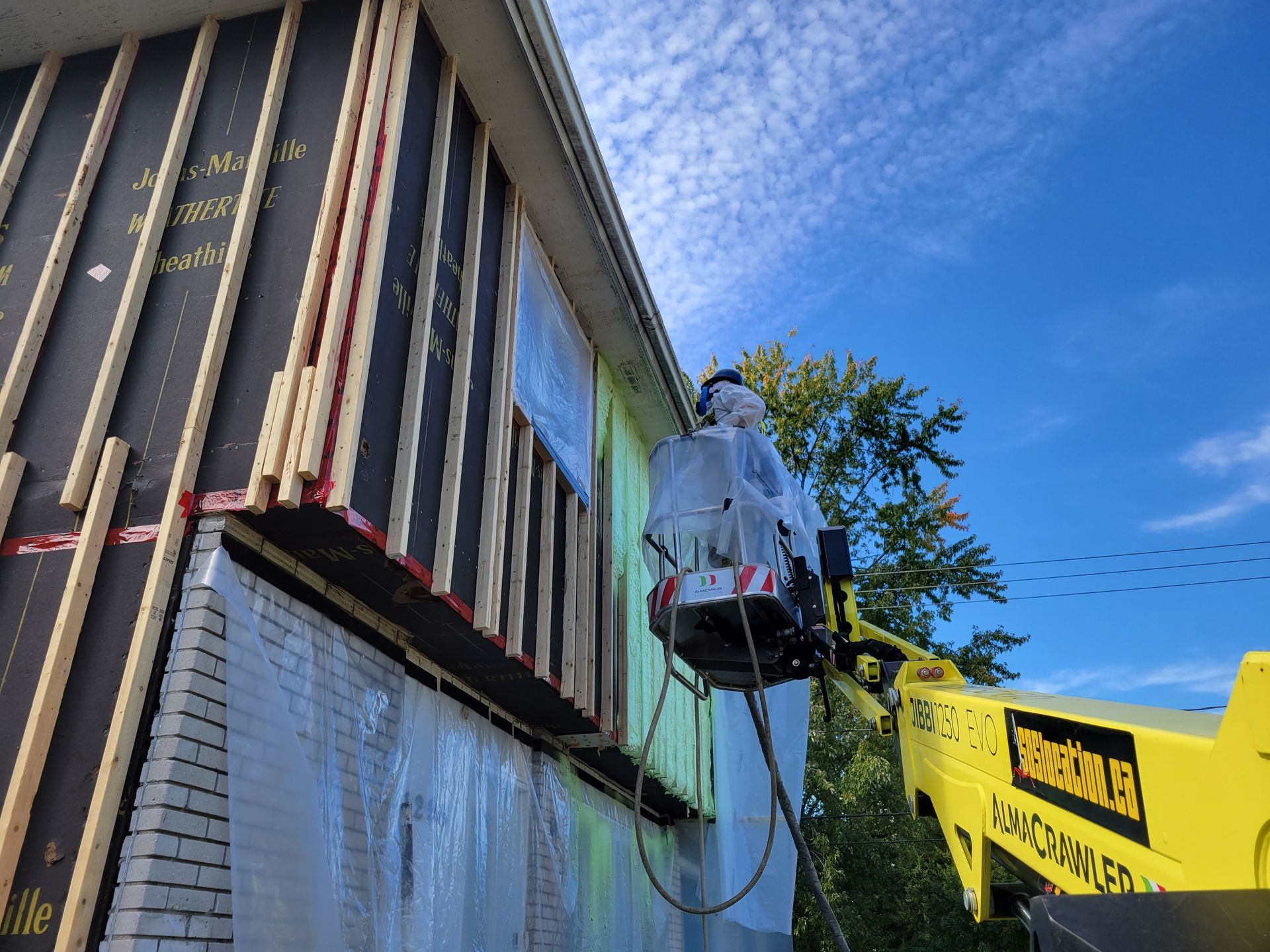 Une personne dans un ascenseur travaille sur le revêtement d'une maison sous un ciel bleu.