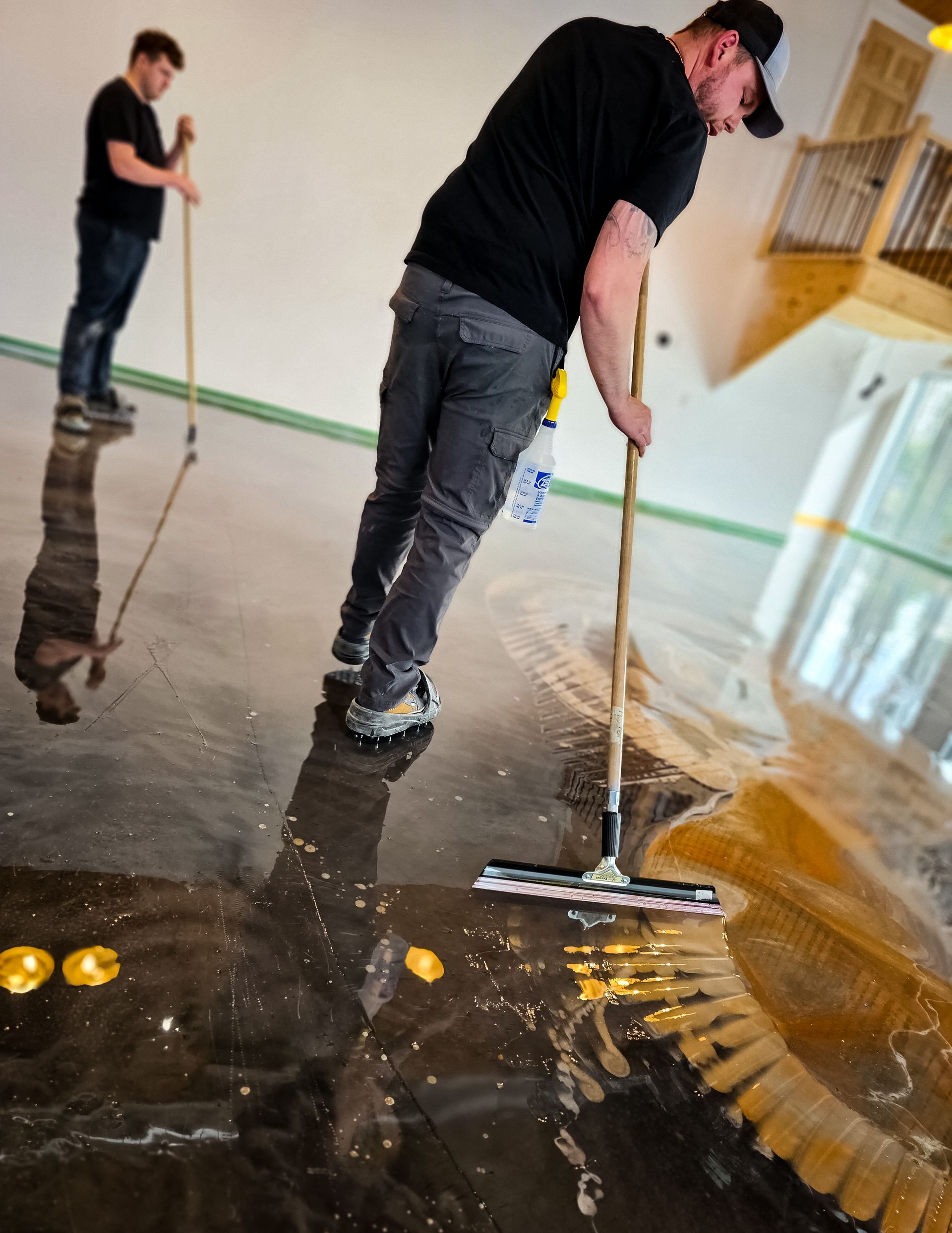Two men applying epoxy to a floor; one in the foreground using a squeegee, the other in the background with a roller.