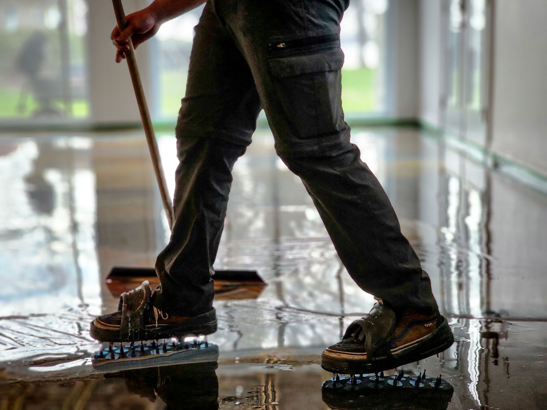 Person in work clothes, spikes on their shoes, sweeping a wet, shiny floor.