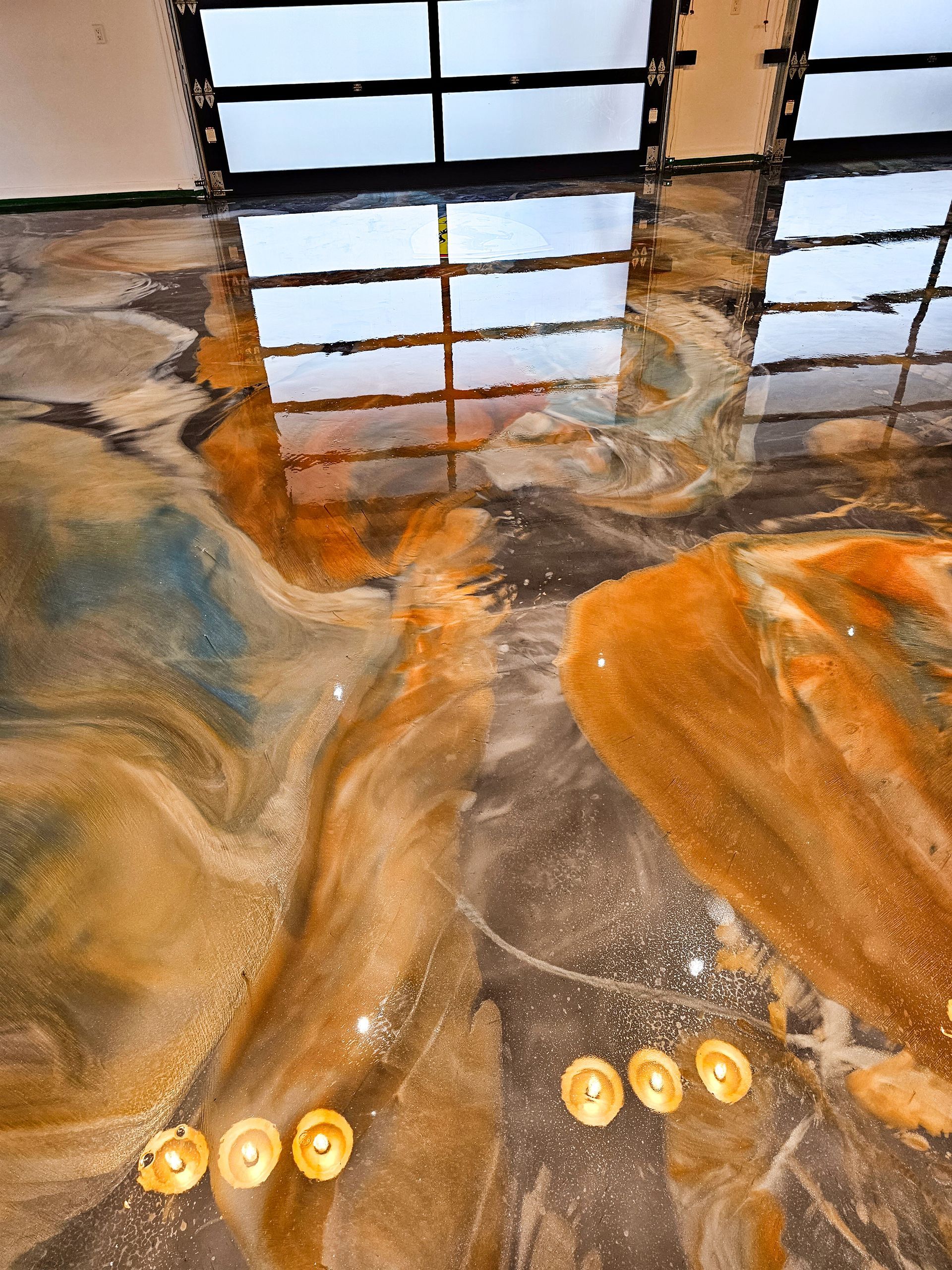Swirled metallic epoxy flooring with gold, brown, and blue hues. Reflective, with glass windows.