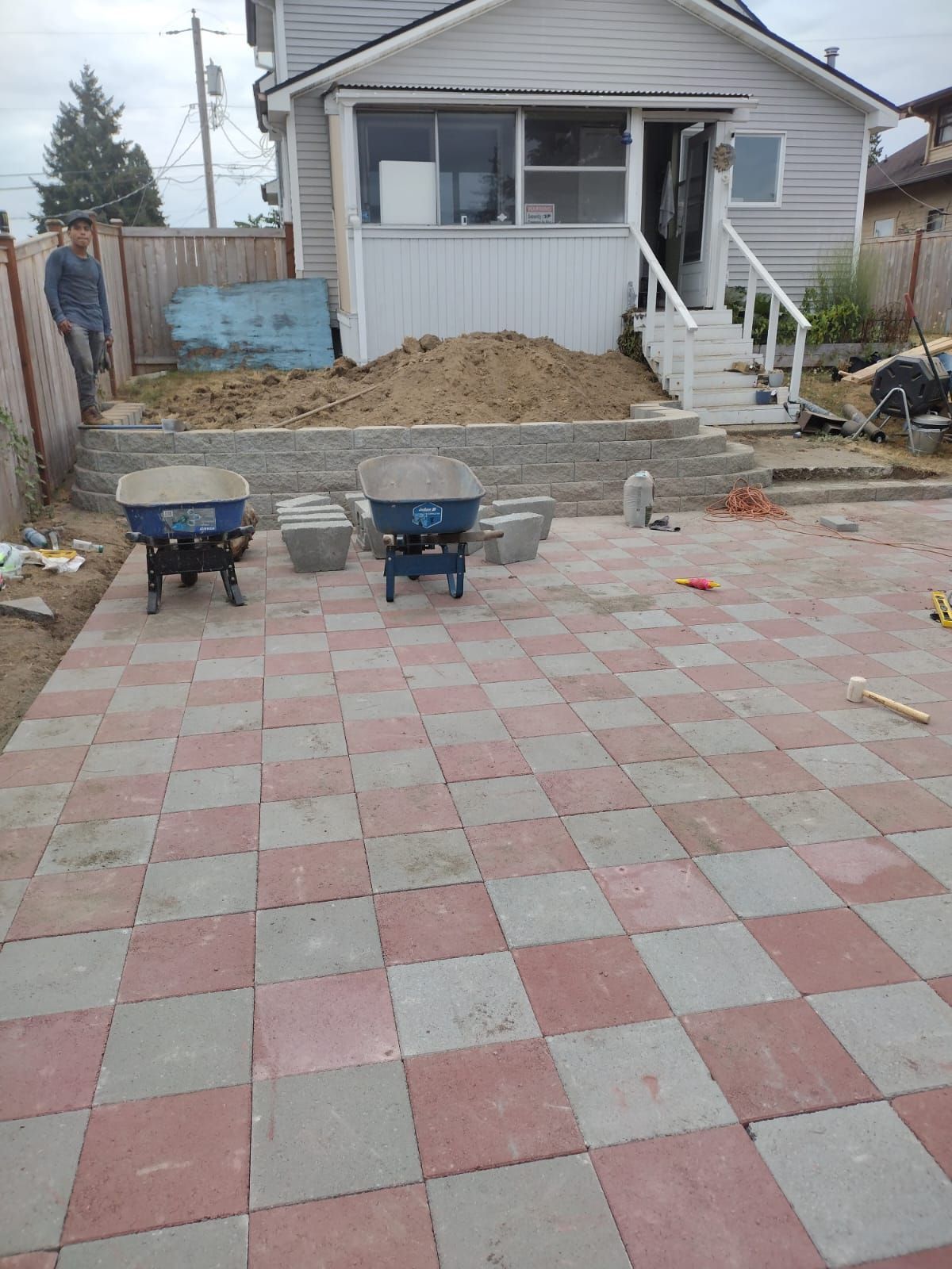 Red and gray checkered patio under construction next to a house. Two people, tools, and materials are visible.