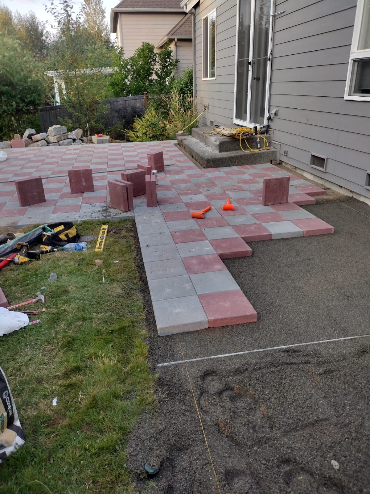 Patio construction, red and gray pavers, level and tools on the ground.