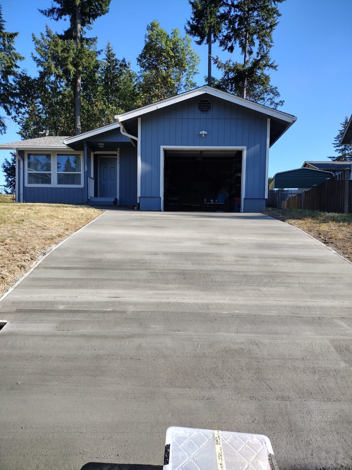 Blue house with open garage and long concrete driveway.