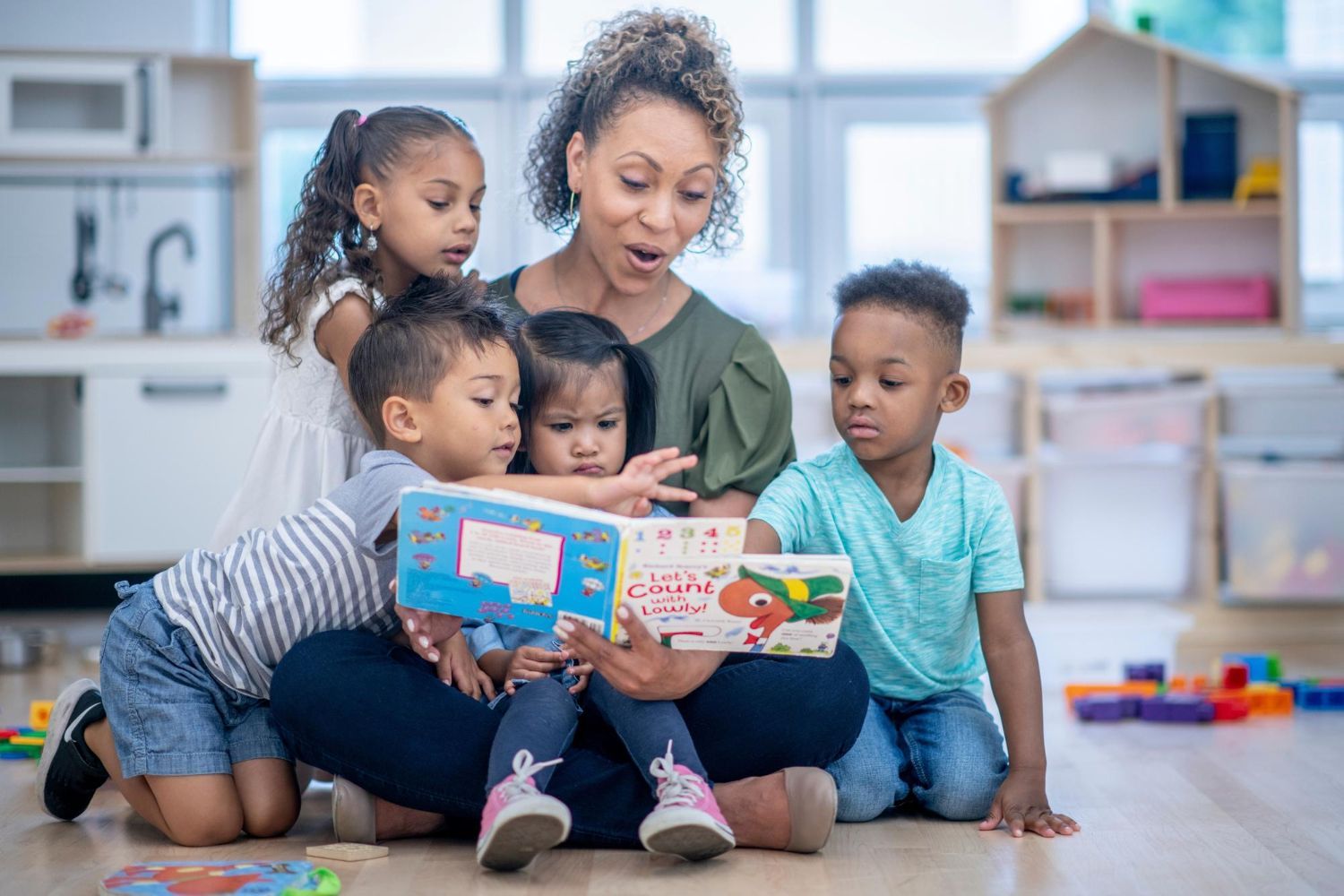 Teacher reading a book to a group of children on the floor.