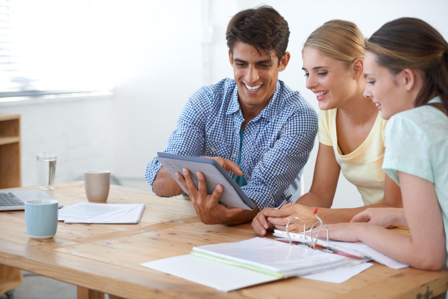 Three people looking at a tablet, smiling, in an office setting.