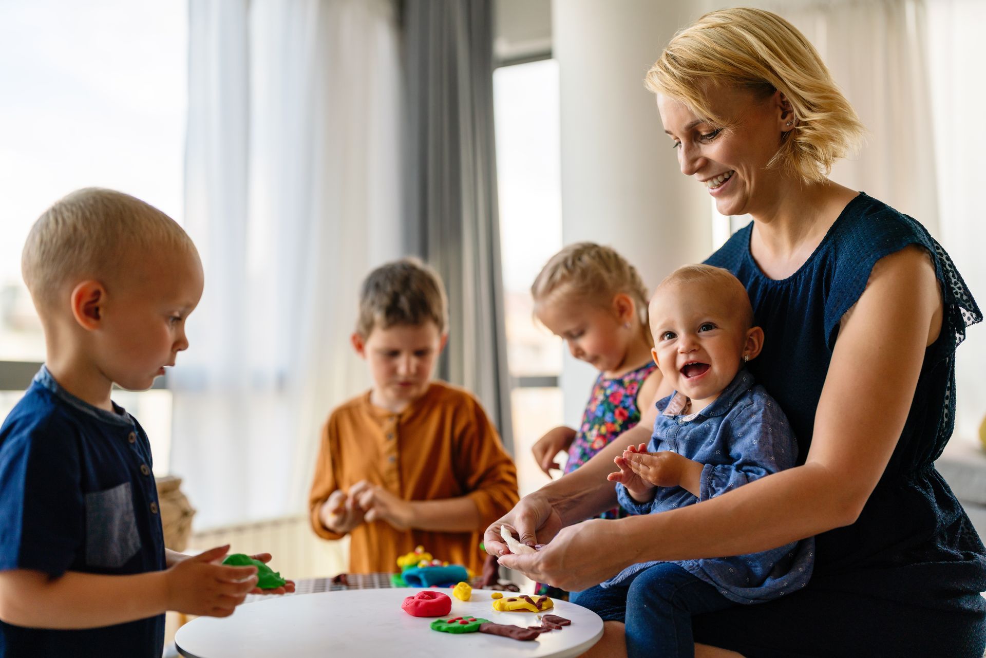 Woman and four young children playing with colorful playdough at a table.