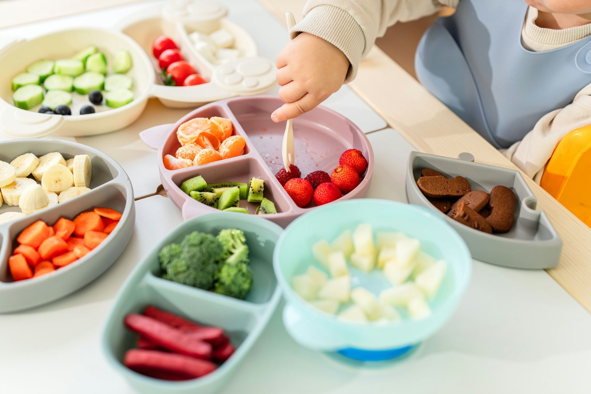 Baby at a high chair reaching for berries on a divided plate with various colorful foods.