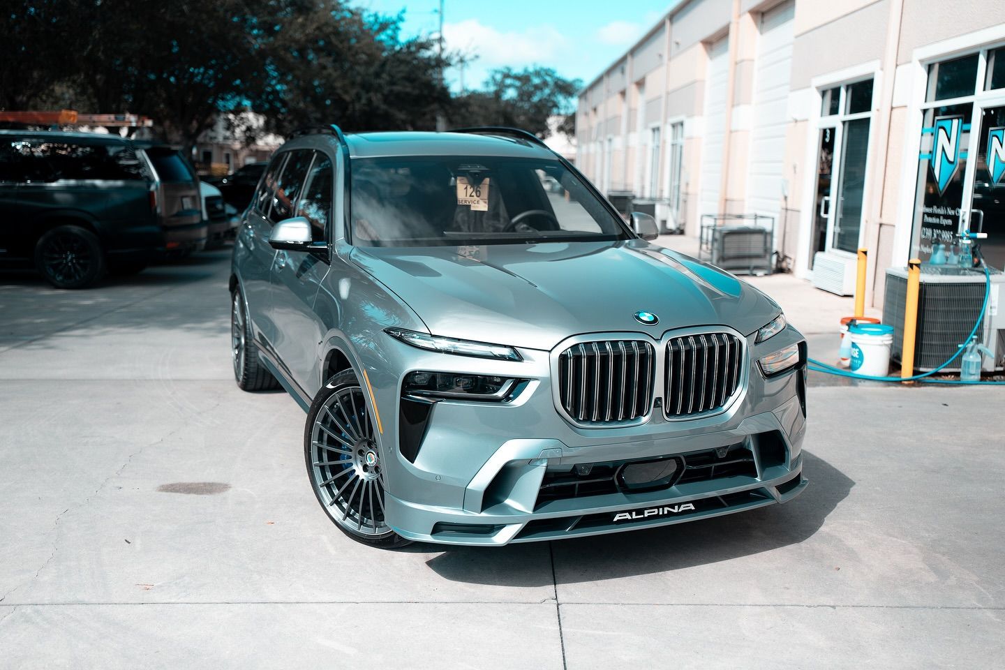 White Porsche 911 GT3 RS with blue accents, parked inside a garage, with logo on wall.