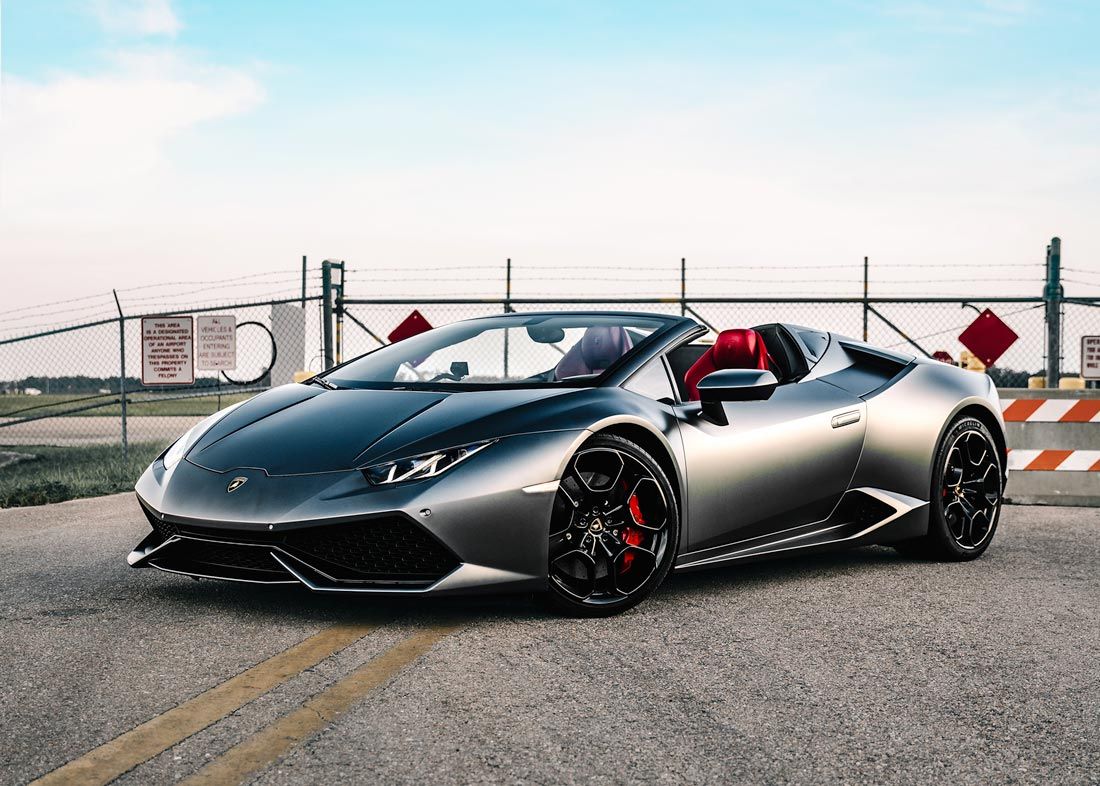 A silver lamborghini huracan convertible is parked on the side of the road.
