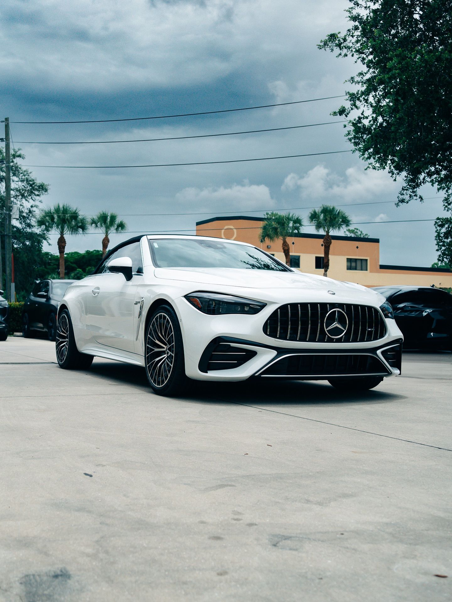 White Mercedes convertible with PPF parked outside an auto shop under a cloudy Florida sky.