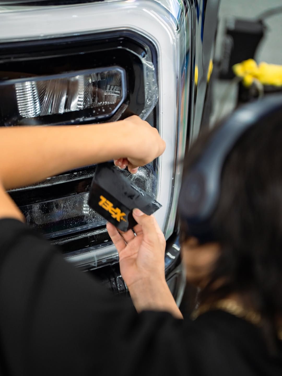 Hand holding a roll of tinted window film next to a car window; shop interior.