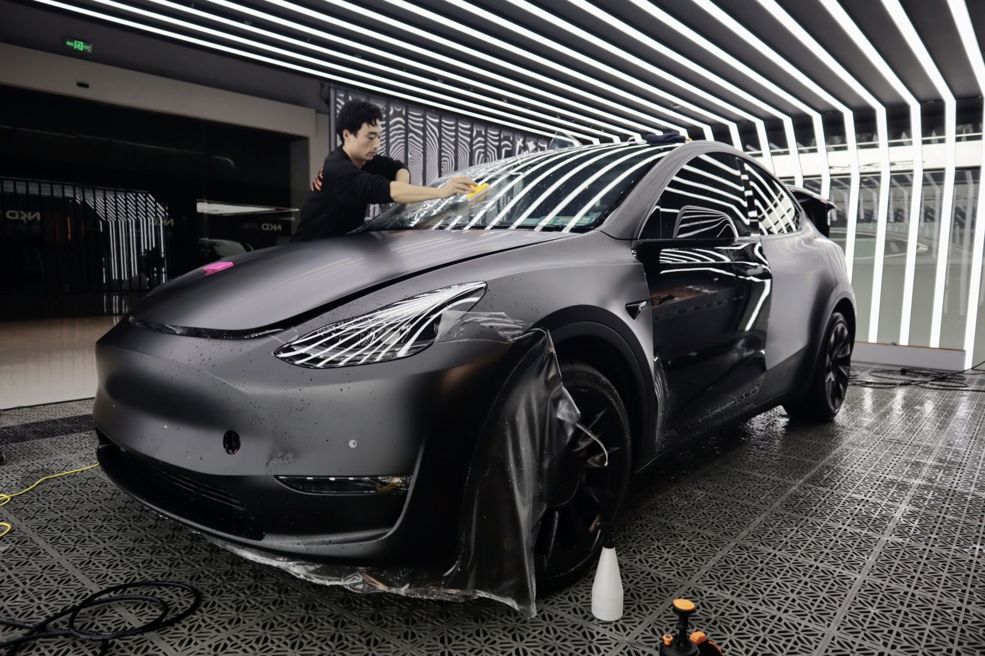 A man is wrapping a tesla model y in a garage.