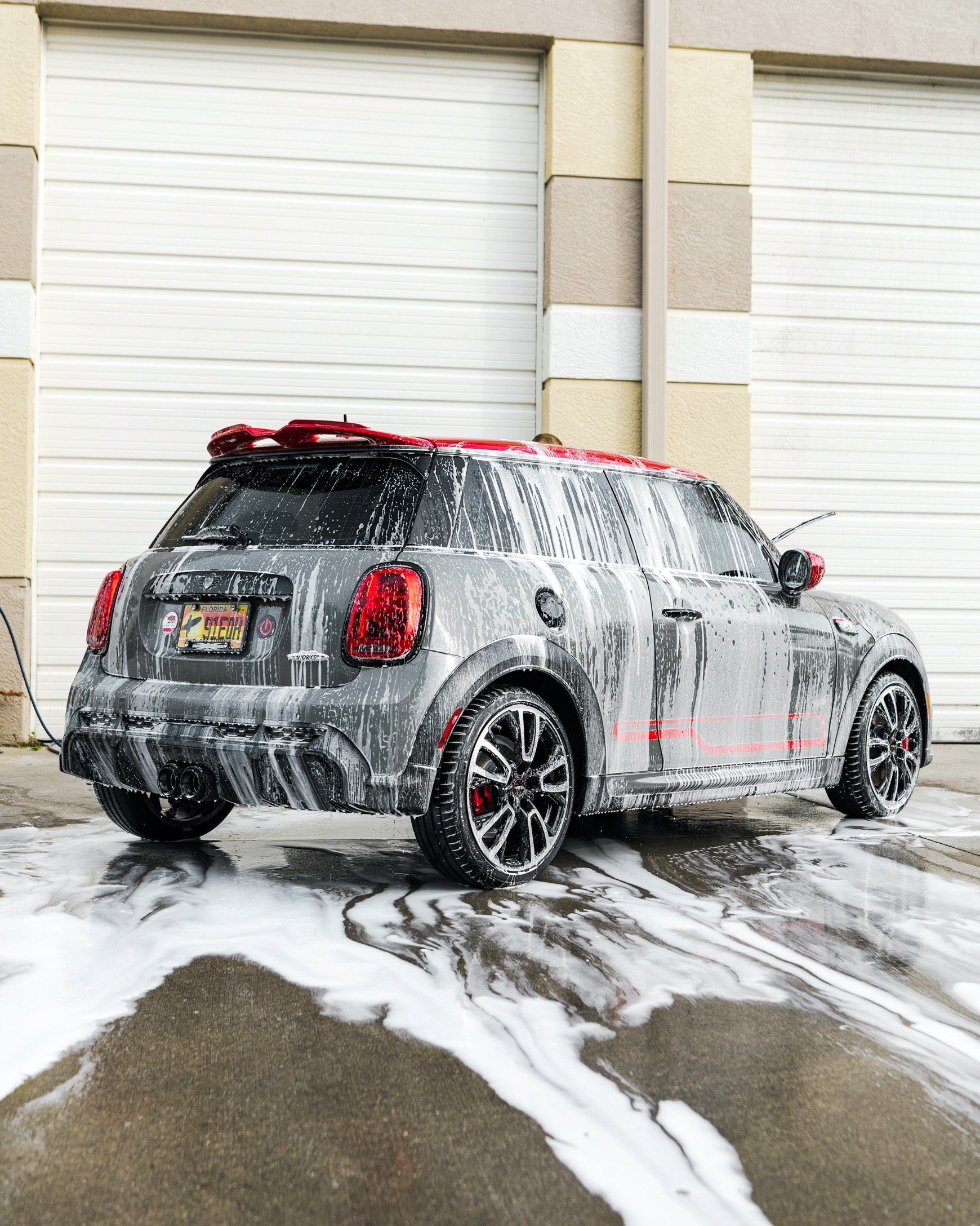 A car is covered in foam in front of a garage.