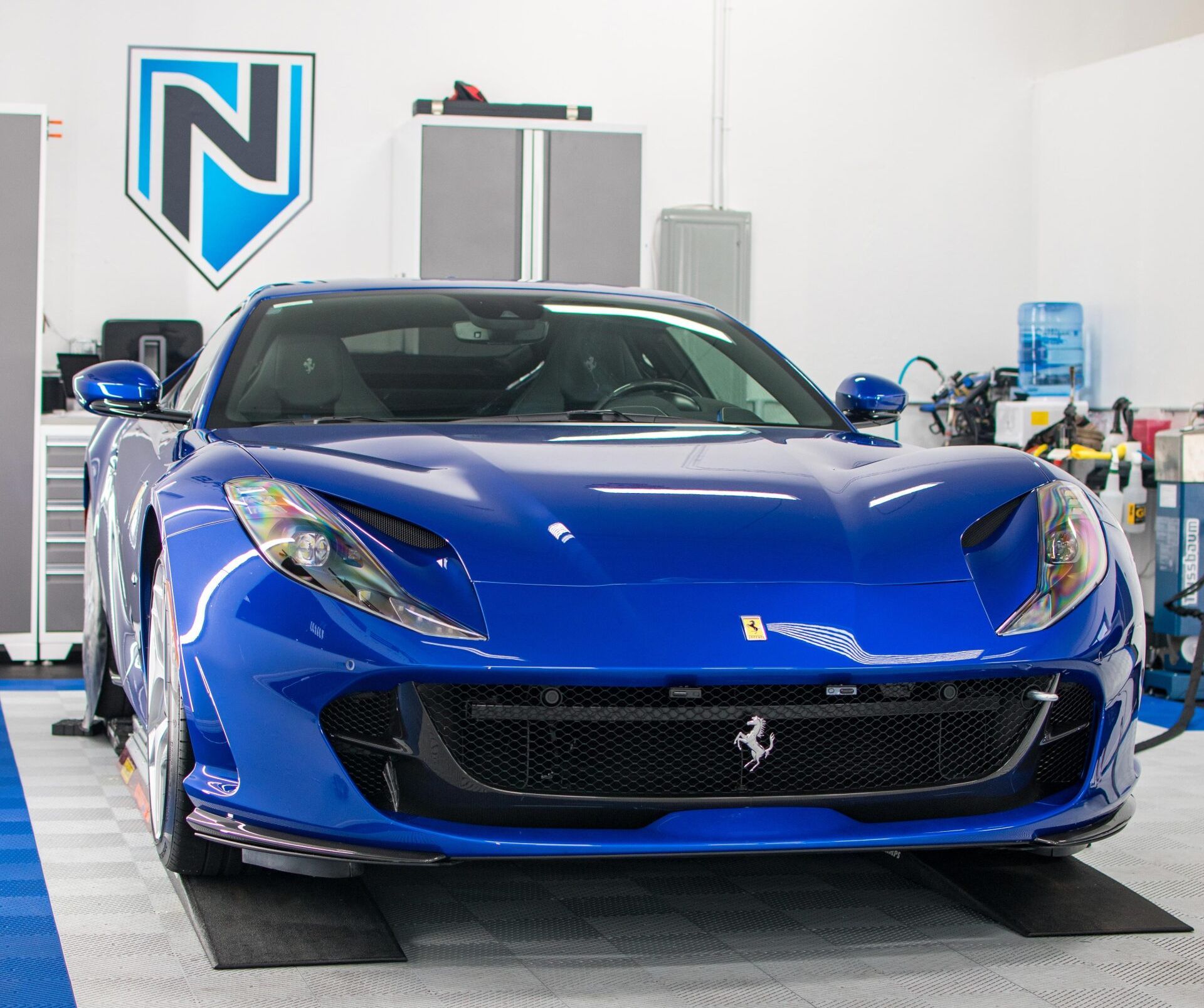 A blue ferrari is parked in a garage with a shield on the wall.
