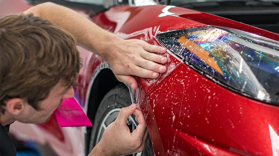 A man is wrapping a red car with a protective film.