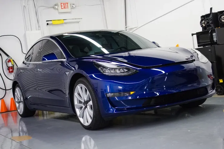 A blue tesla model 3 is parked in a garage.
