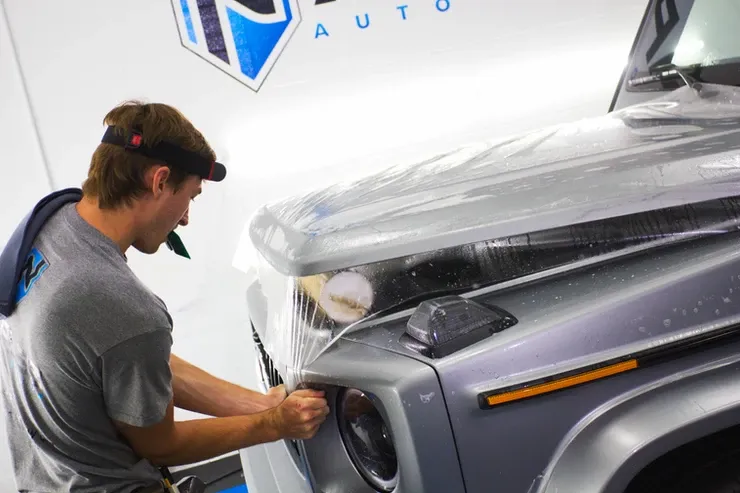 A man is covering the hood of a car with plastic wrap.