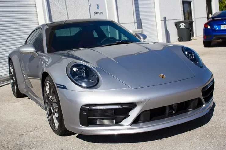 A silver porsche is parked in front of a building