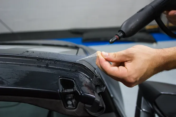 A person is applying a clear film to a car windshield.