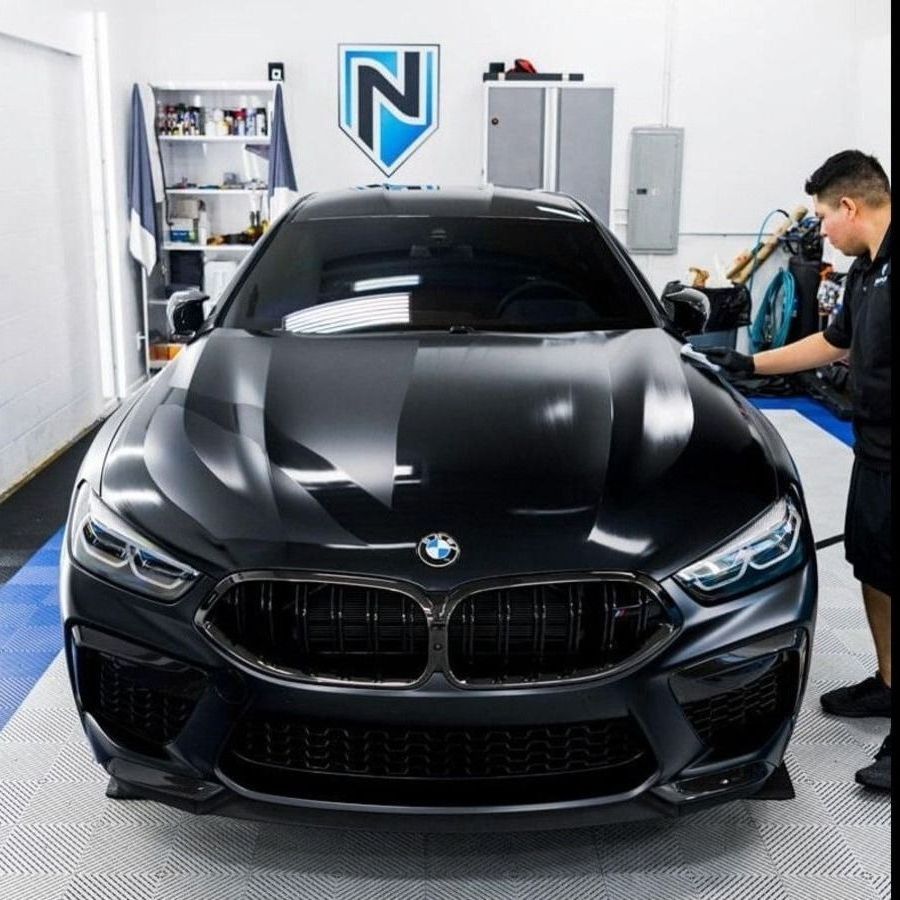 Black BMW being detailed in a garage. A person is working on the car.