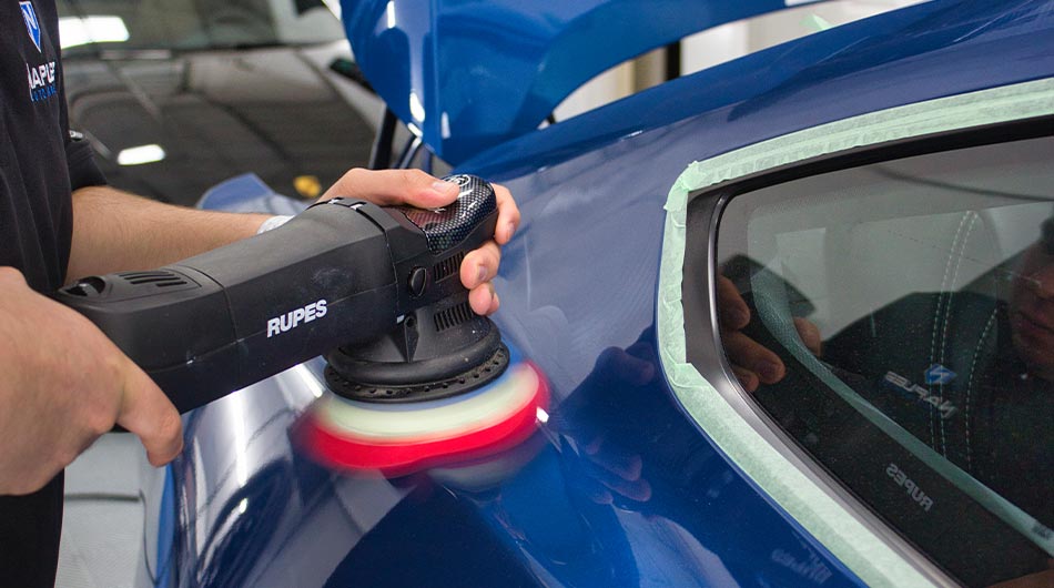 A person is polishing a blue car with a machine.
