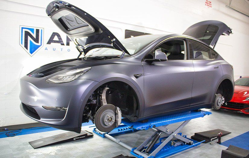 A tesla model y is sitting on a lift with its hood open.