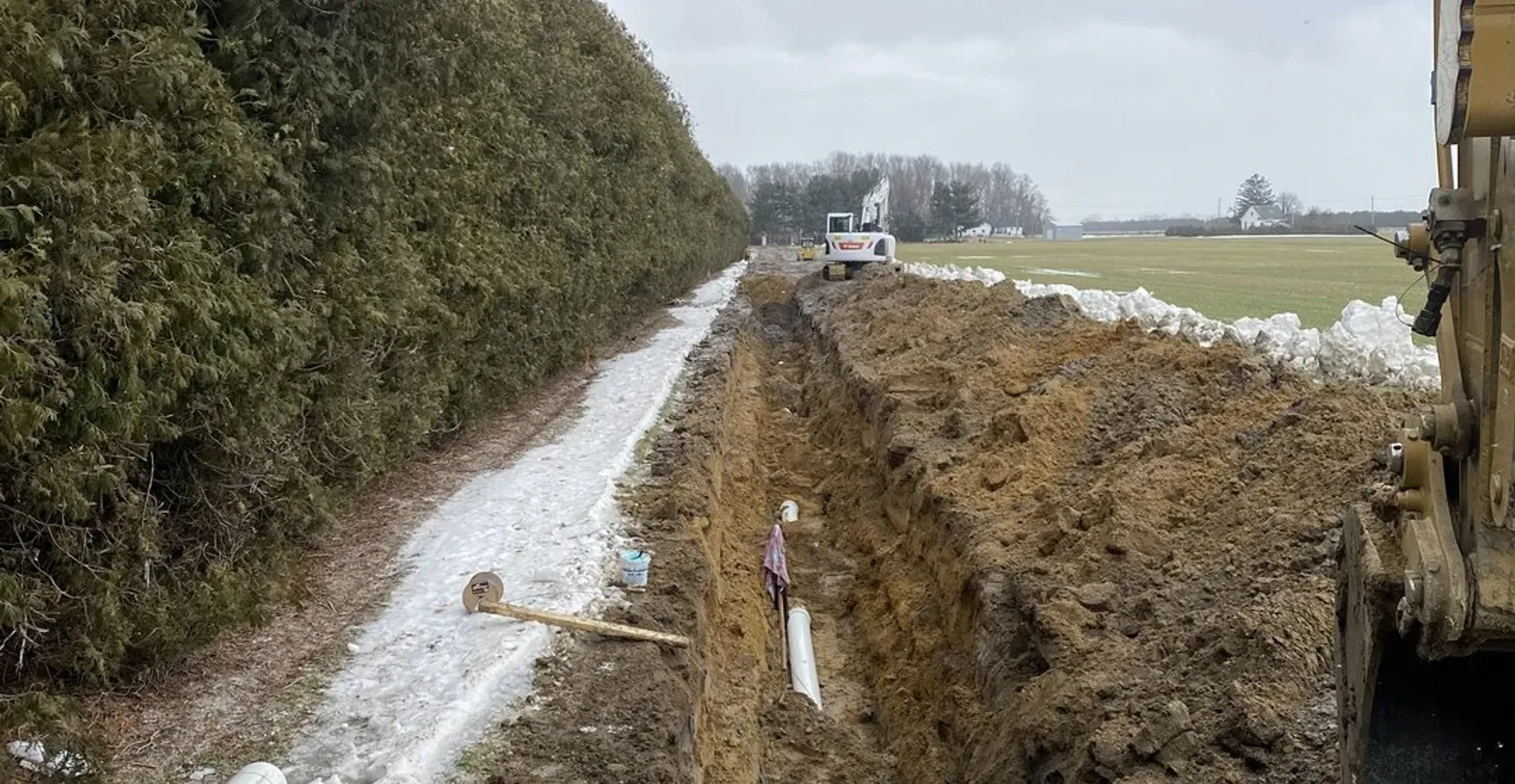 A bulldozer is digging a trench on the side of a road.