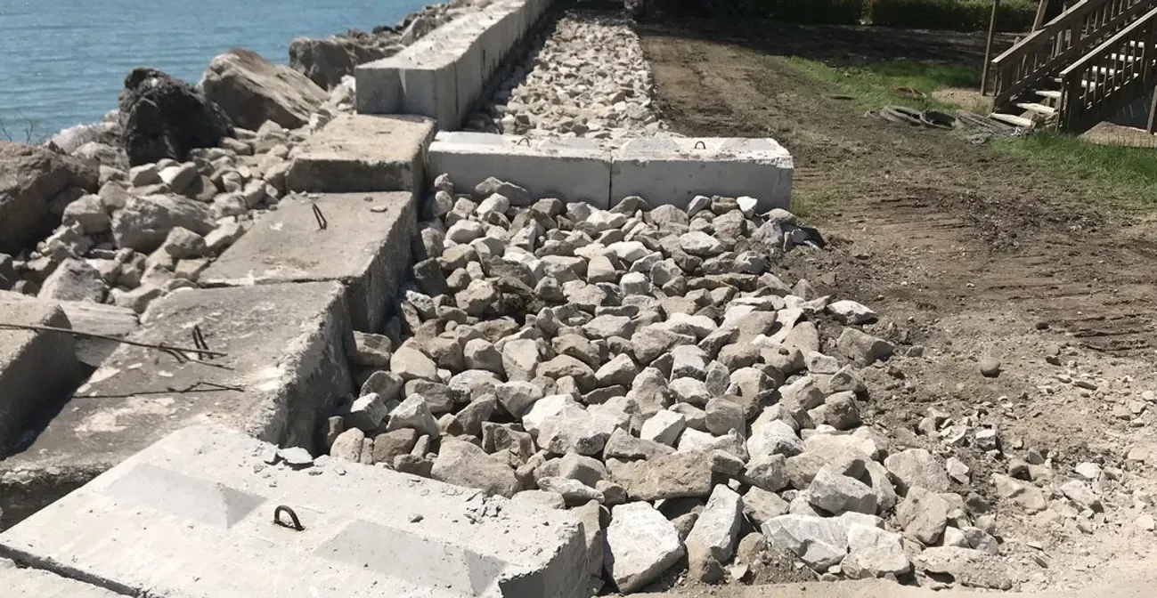 A pile of rocks is sitting on the ground next to a body of water.