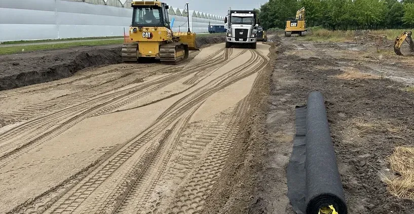 A bulldozer is driving down a dirt road next to a truck.