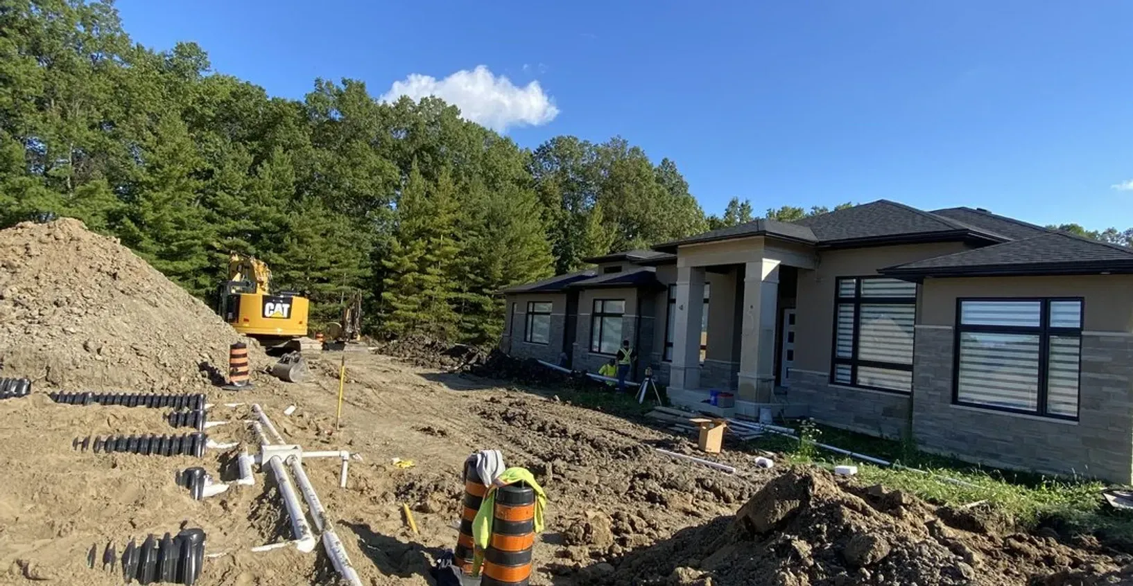 A construction site with a large pile of dirt in front of a house under construction.