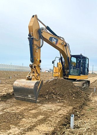 A yellow excavator is digging a hole in a dirt field.