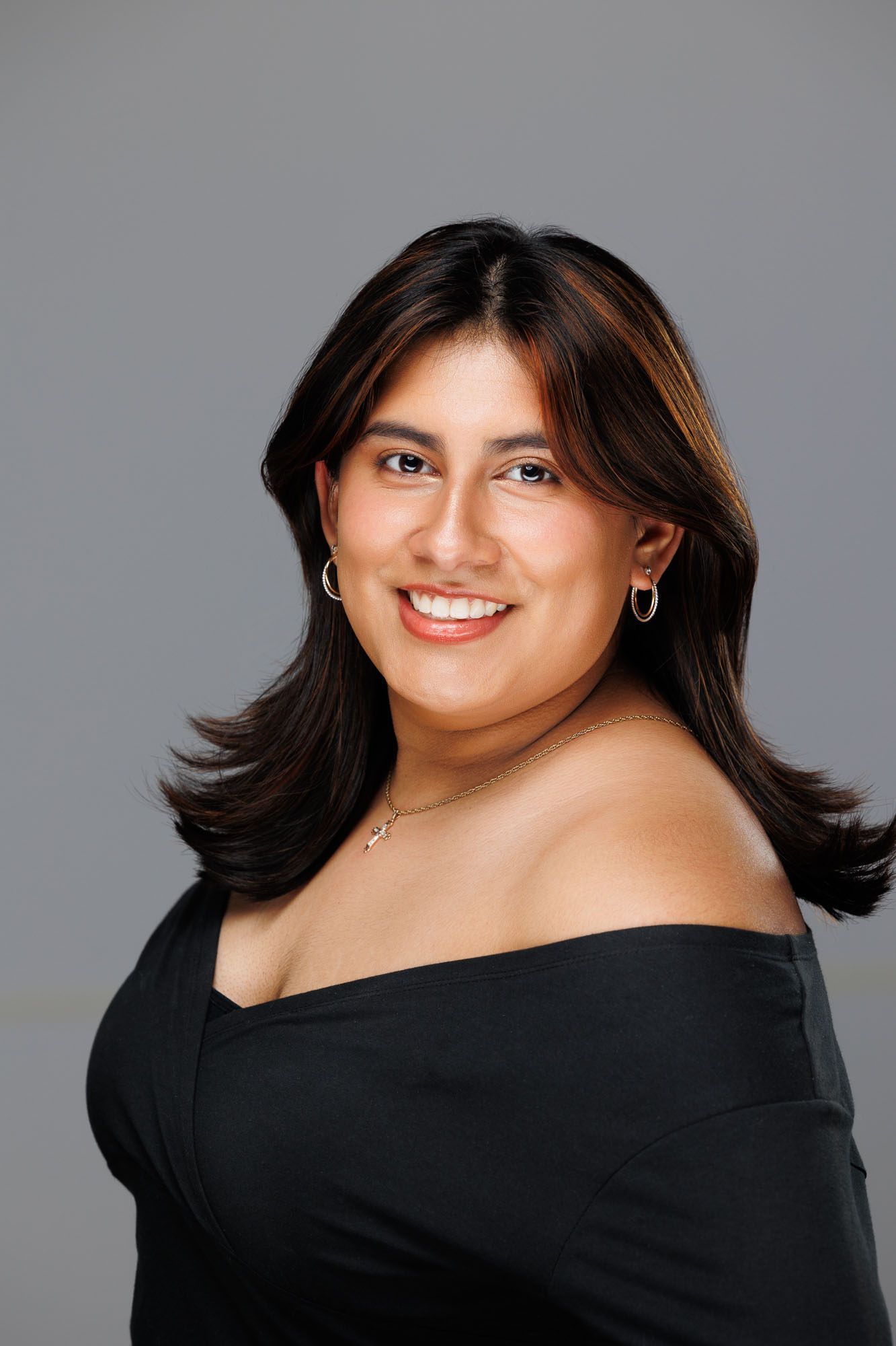A woman in a black off the shoulder top is smiling for the camera.