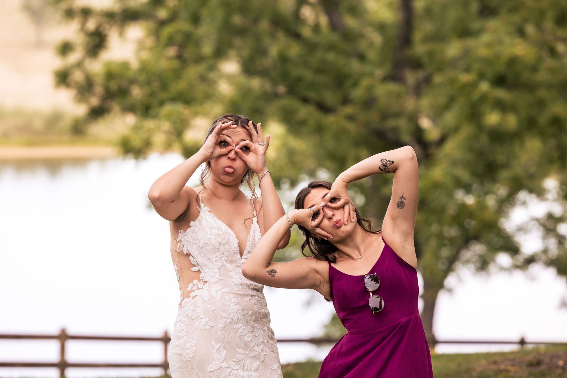 A bride and her bridesmaid are making funny faces with their hands.