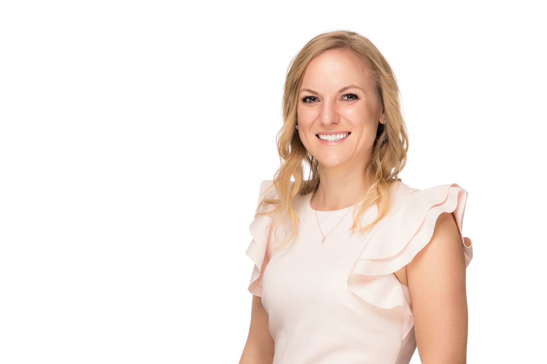 A woman in a pink dress is smiling for the camera on a white background.