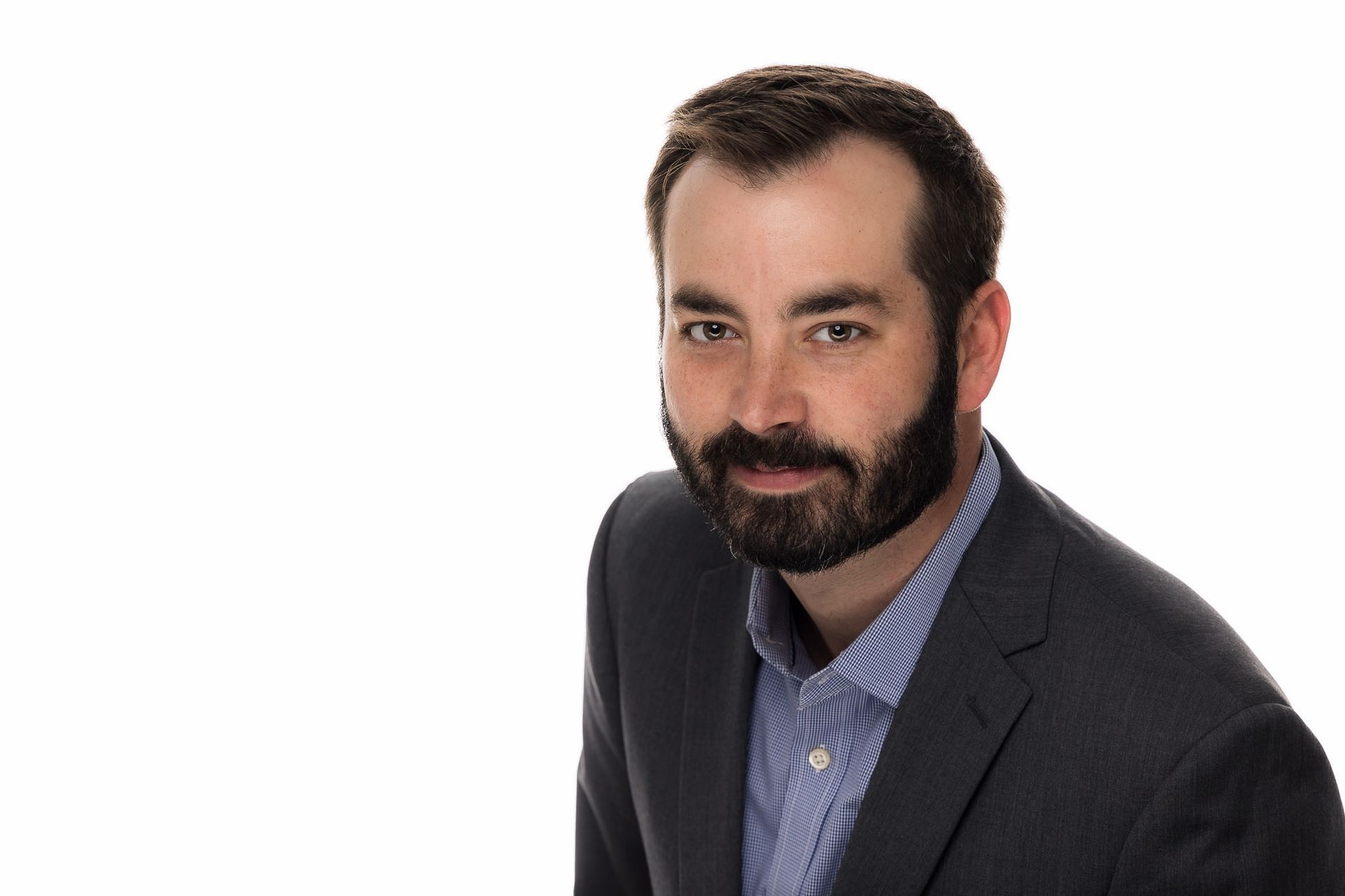 A man with a beard is wearing a suit and a blue shirt.