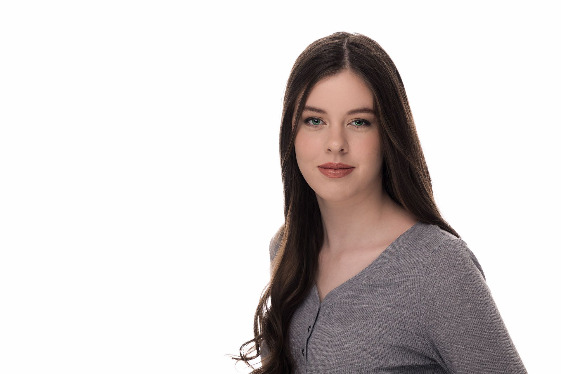 A young woman with long hair is wearing a grey sweater and looking at the camera.