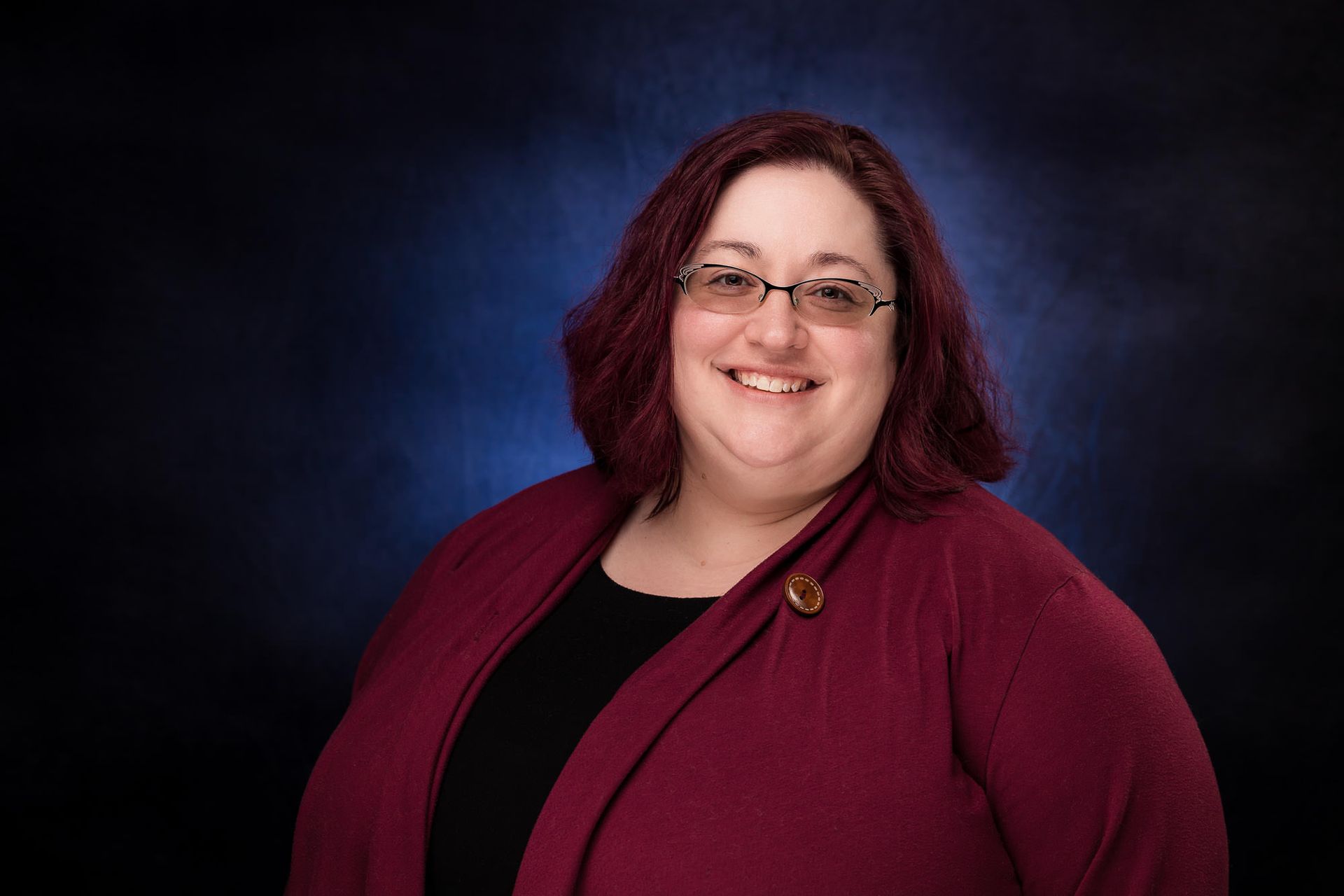 A woman wearing glasses and a red sweater is smiling for the camera.