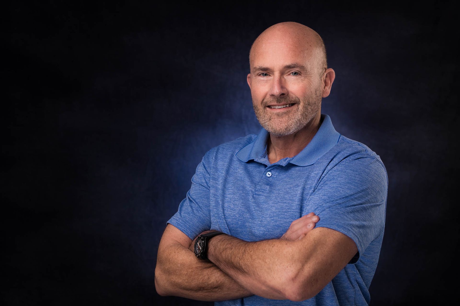 A man in a blue shirt is standing with his arms crossed.