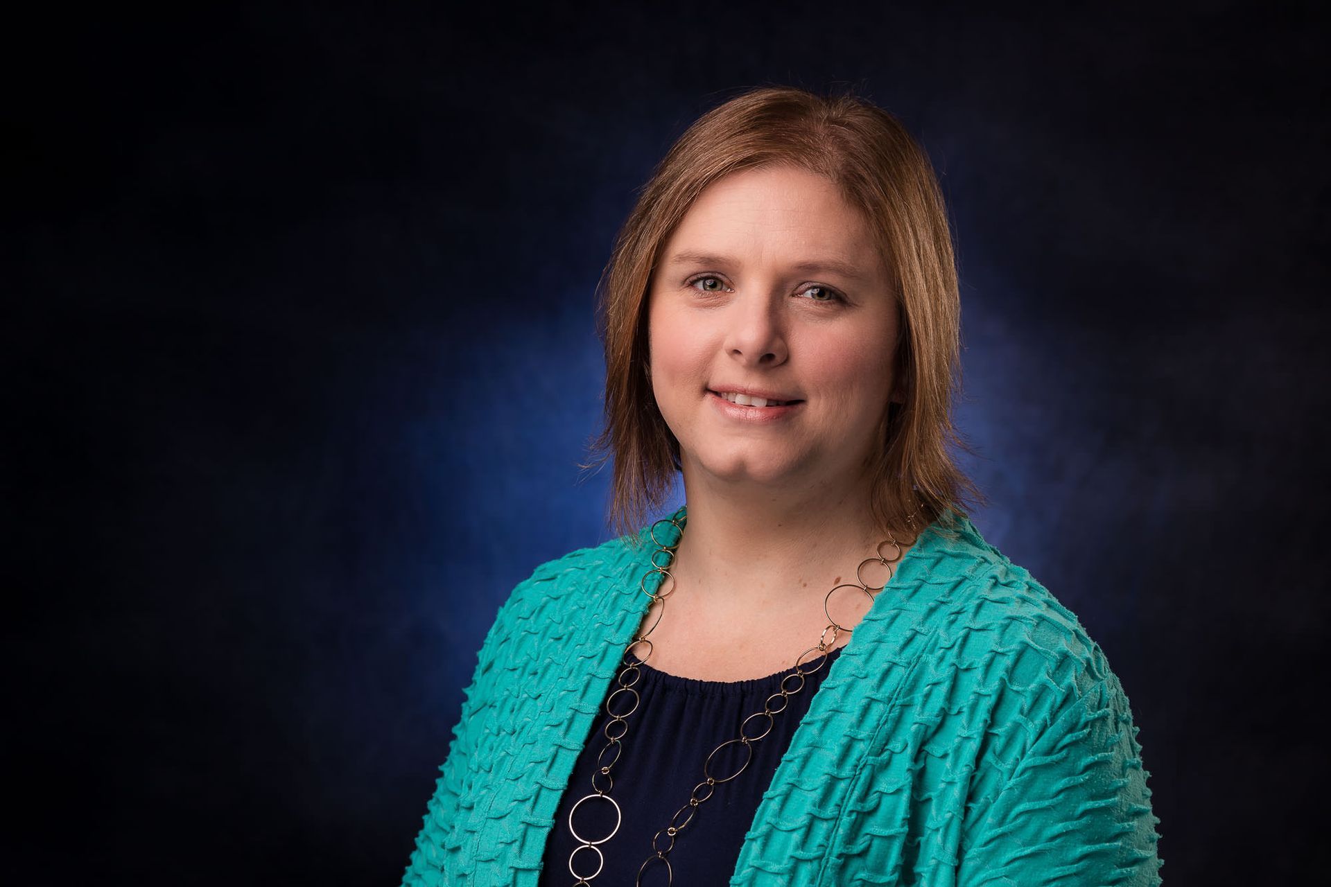A woman wearing a blue sweater and a necklace is smiling for the camera.