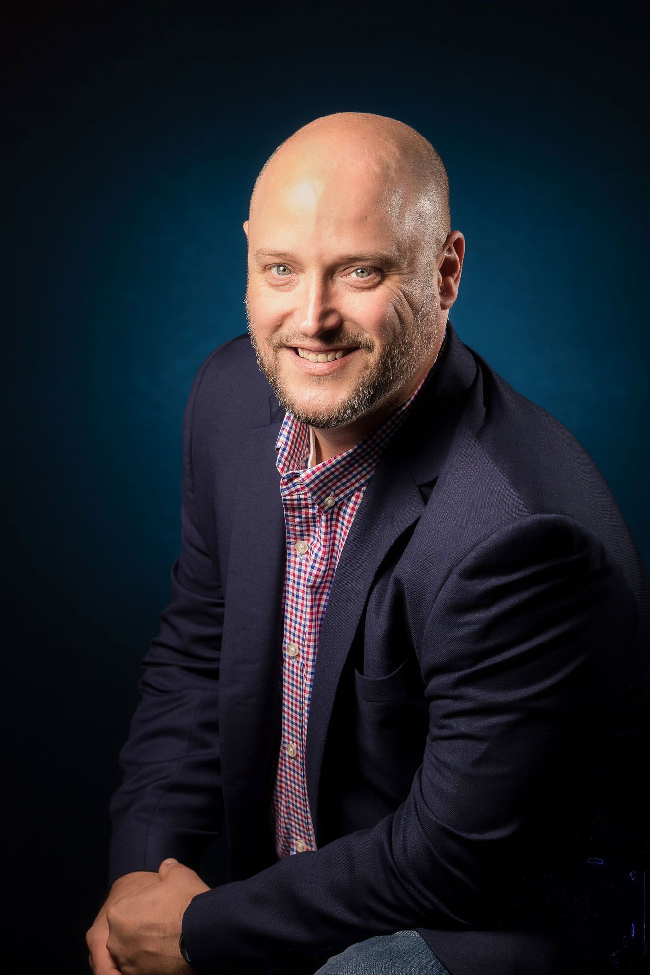 A bald man in a suit and tie is smiling for the camera.