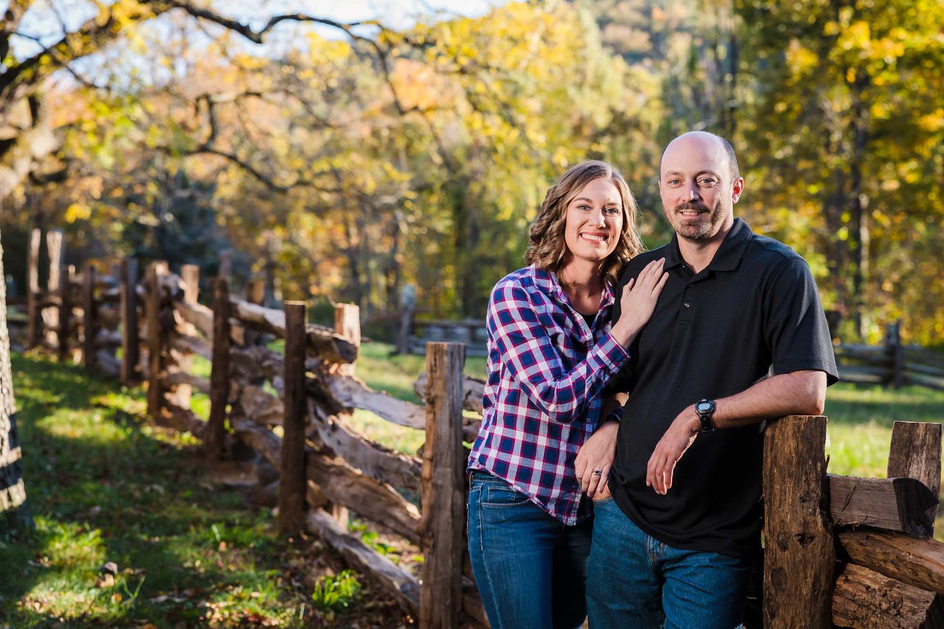 A man and a woman are standing next to a wooden fence.