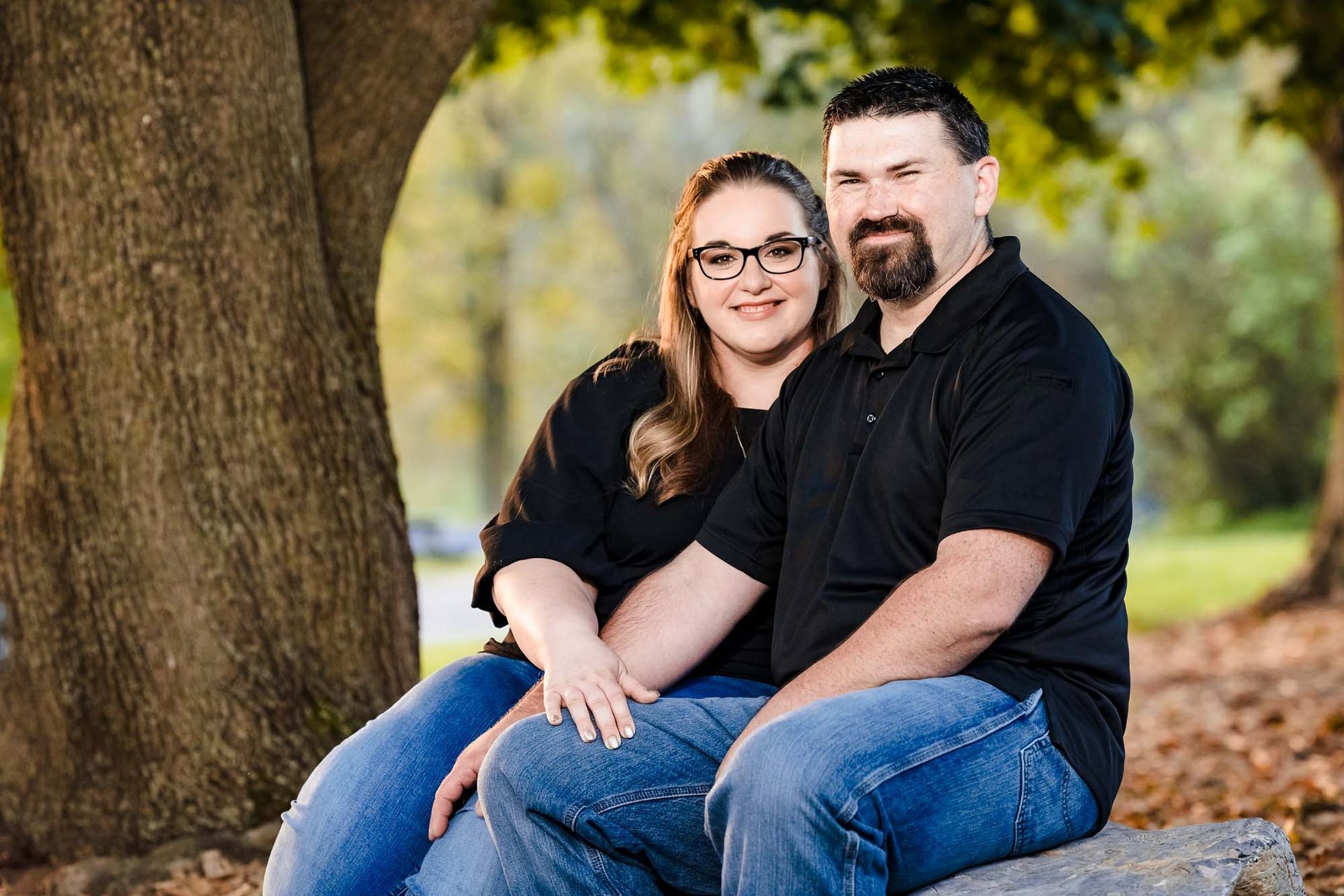 A man and a woman are sitting on a rock under a tree.