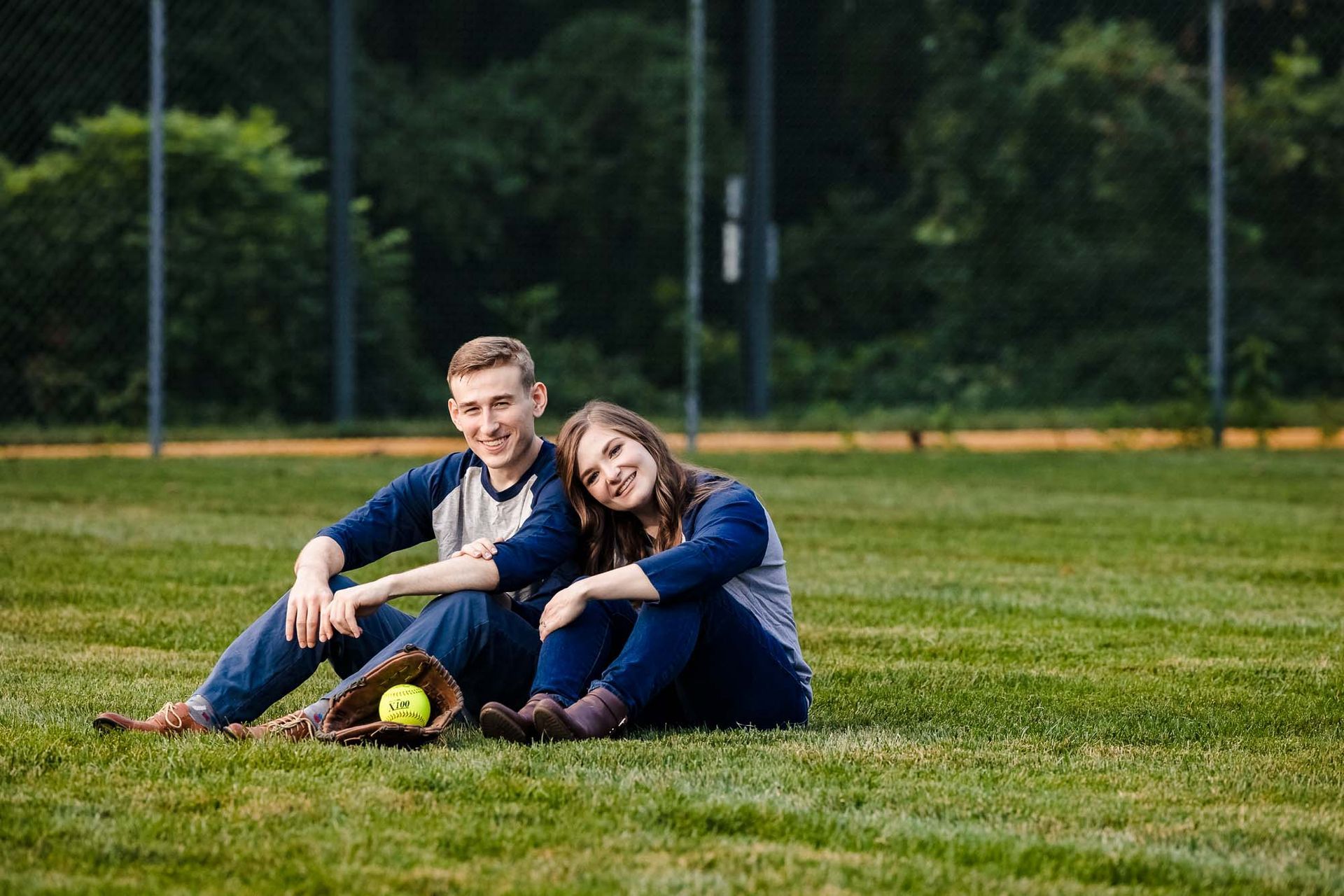 A man and a woman are sitting on the grass with a softball.