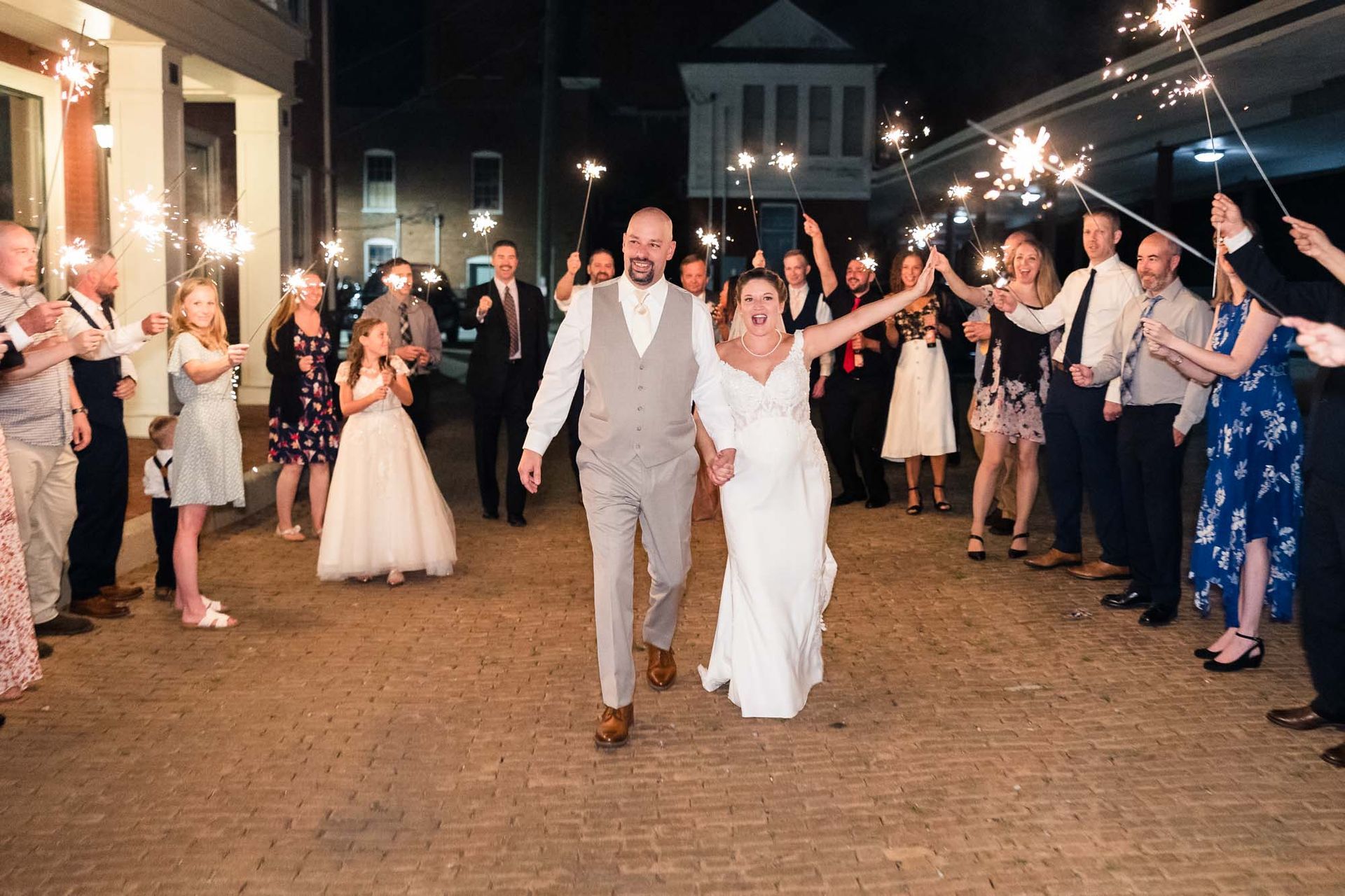 A bride and groom are walking through a tunnel of sparklers.