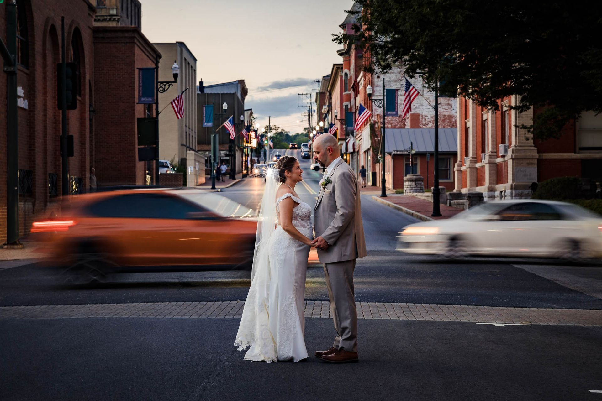 A bride and groom are standing in the middle of a city street holding hands.