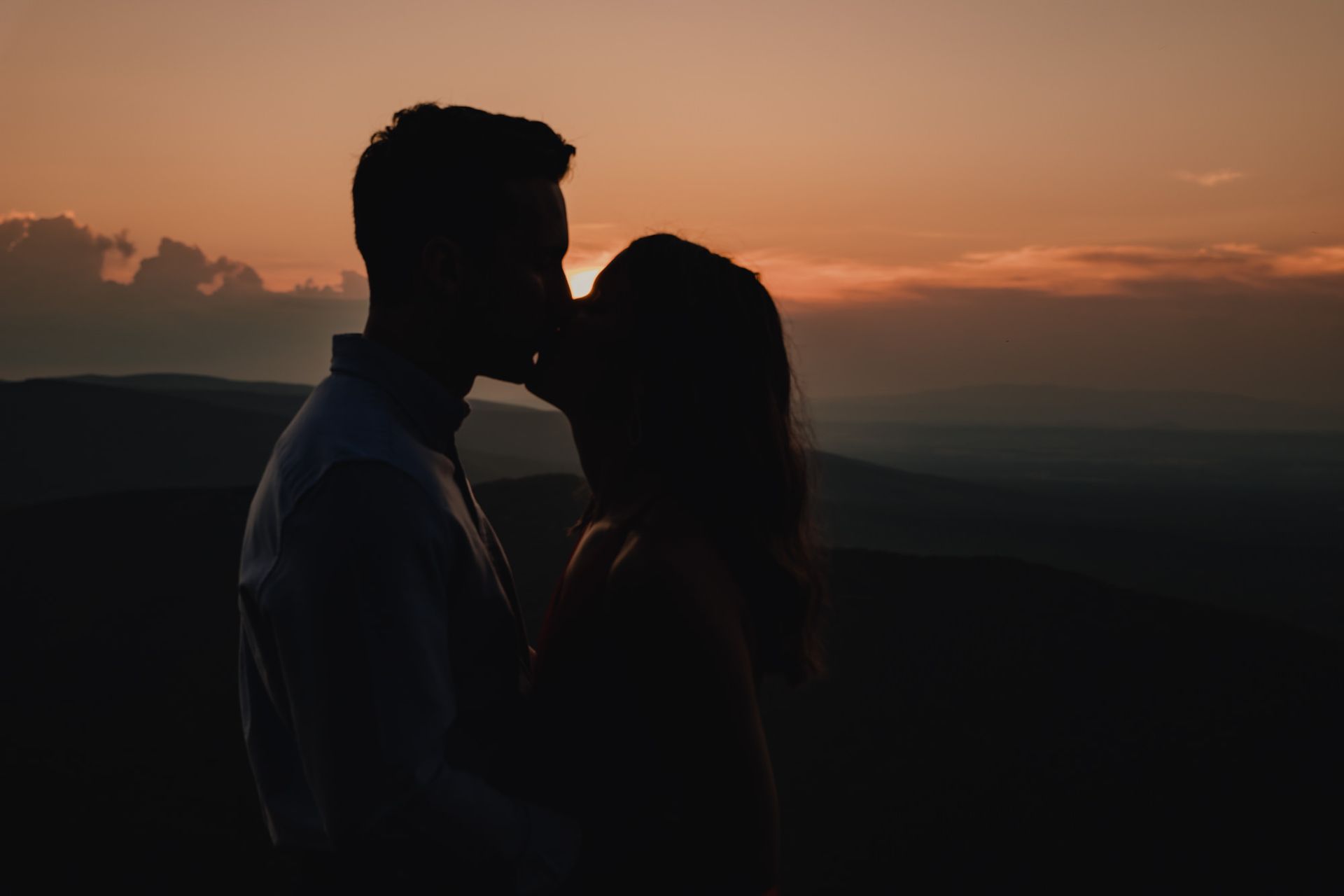A man and a woman are kissing in front of a sunset.