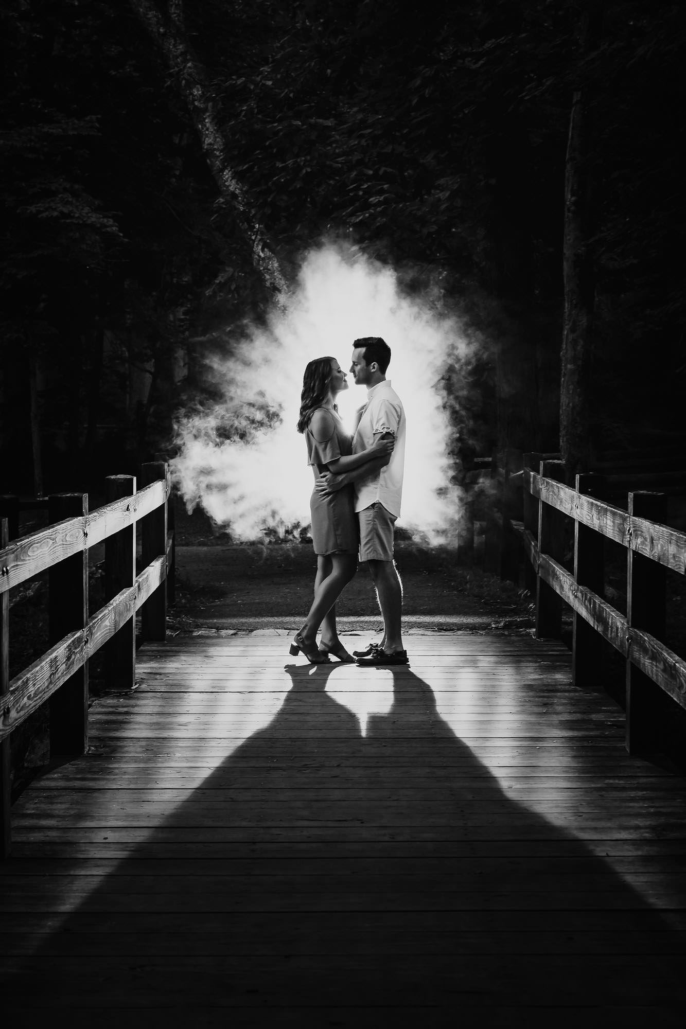 A black and white photo of a man and woman kissing on a wooden bridge.