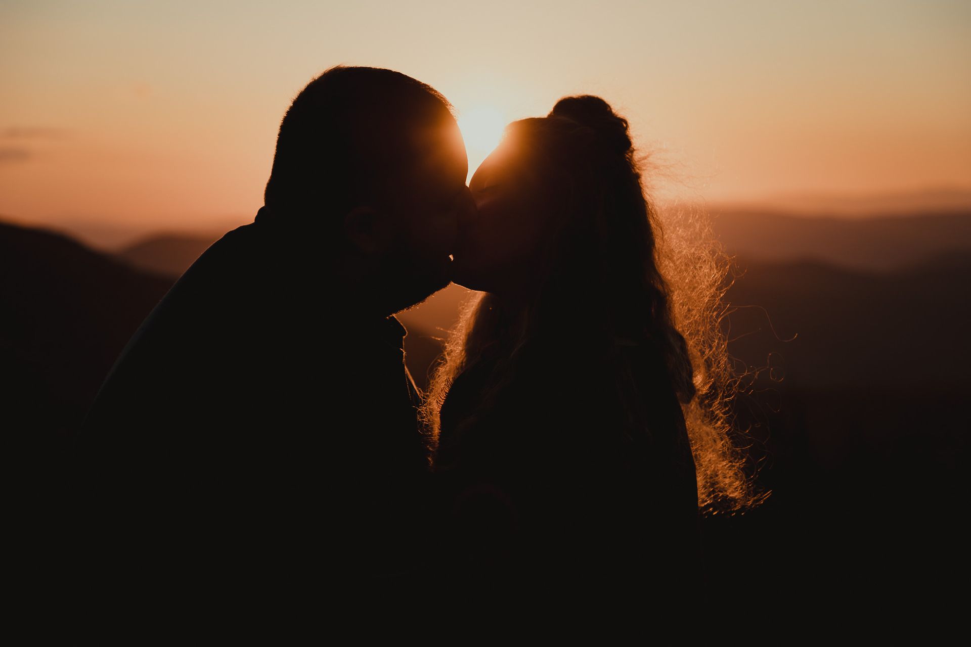 A man and a woman are kissing at sunset.