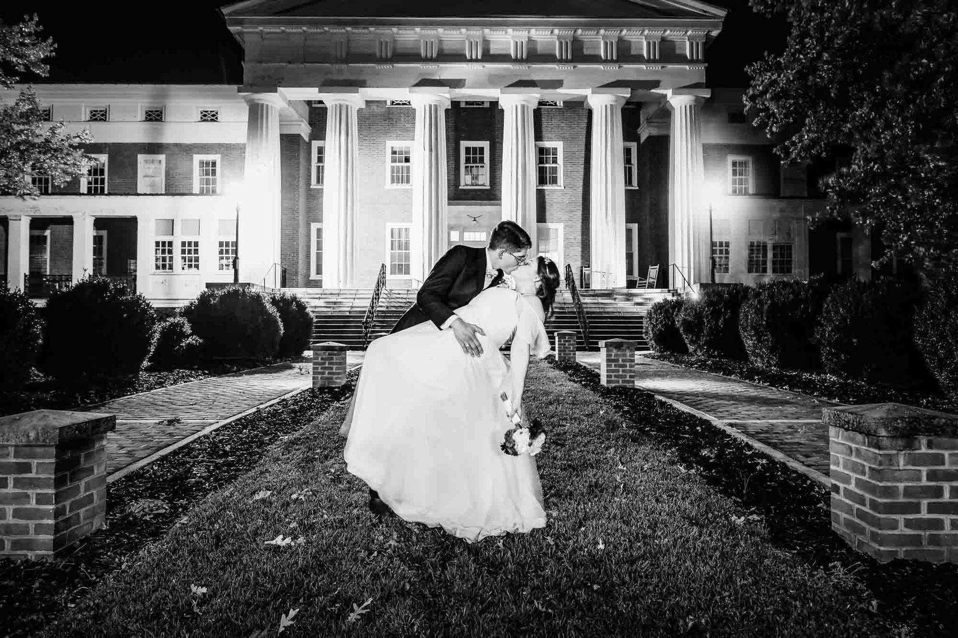 A bride and groom are kissing in front of a large building at night.
