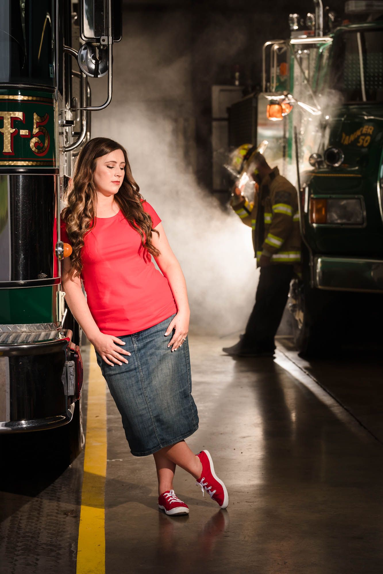 A woman in a red shirt and denim skirt is standing in front of a fire truck.